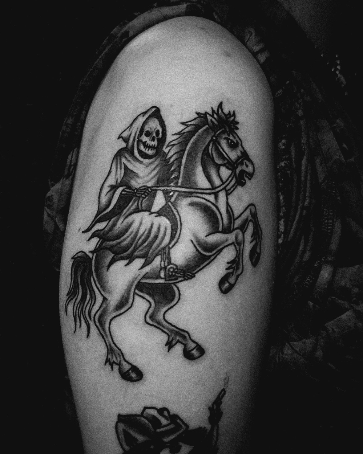 A black and gray tattoo on a person's arm depicting a skeletal figure in a hooded cloak riding a horse. Brooke Desieus tattoo.