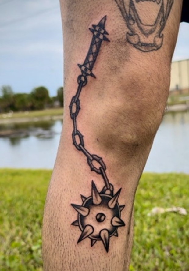 A detailed tattoo on a person's leg featuring a spiked ball connected by a chain.